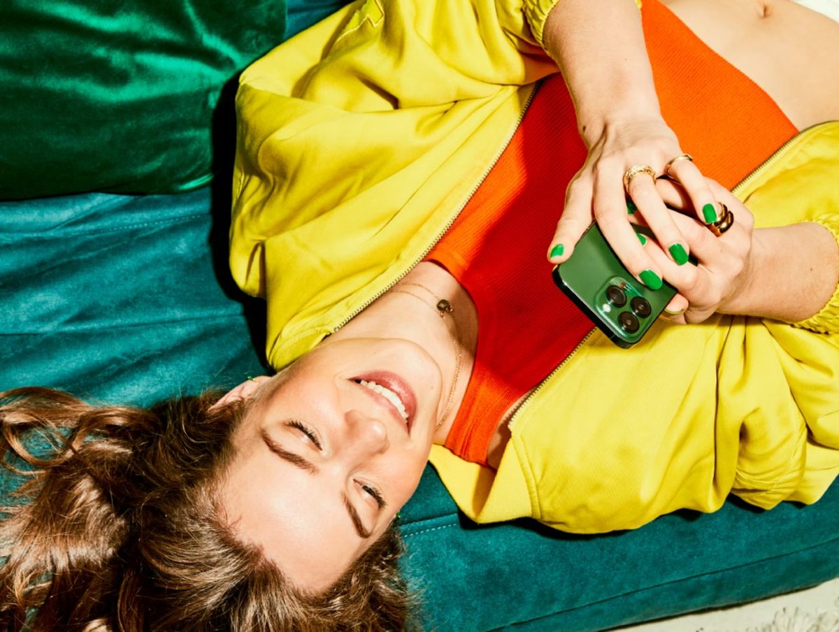 Een lachende vrouw op een bank met een groene telefoon in haar hand